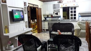 Una sala de estar con televisor, un comedor con sillas, una cocina con microondas y una ventana.