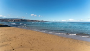Una playa con agua azul cristalina, orilla arenosa y colinas al fondo.