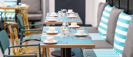 A modern dining area with tables set for a meal, chairs, and a sofa with striped cushions.