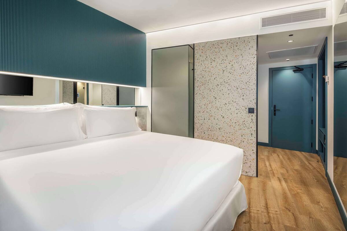 Una habitación de hotel moderna con una cama grande, un espejo, un armario y una puerta que da a un baño.