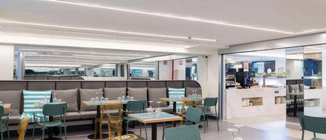 A modern restaurant with a seating area featuring sofas and tables, a counter with a display case, and a clean, contemporary design.