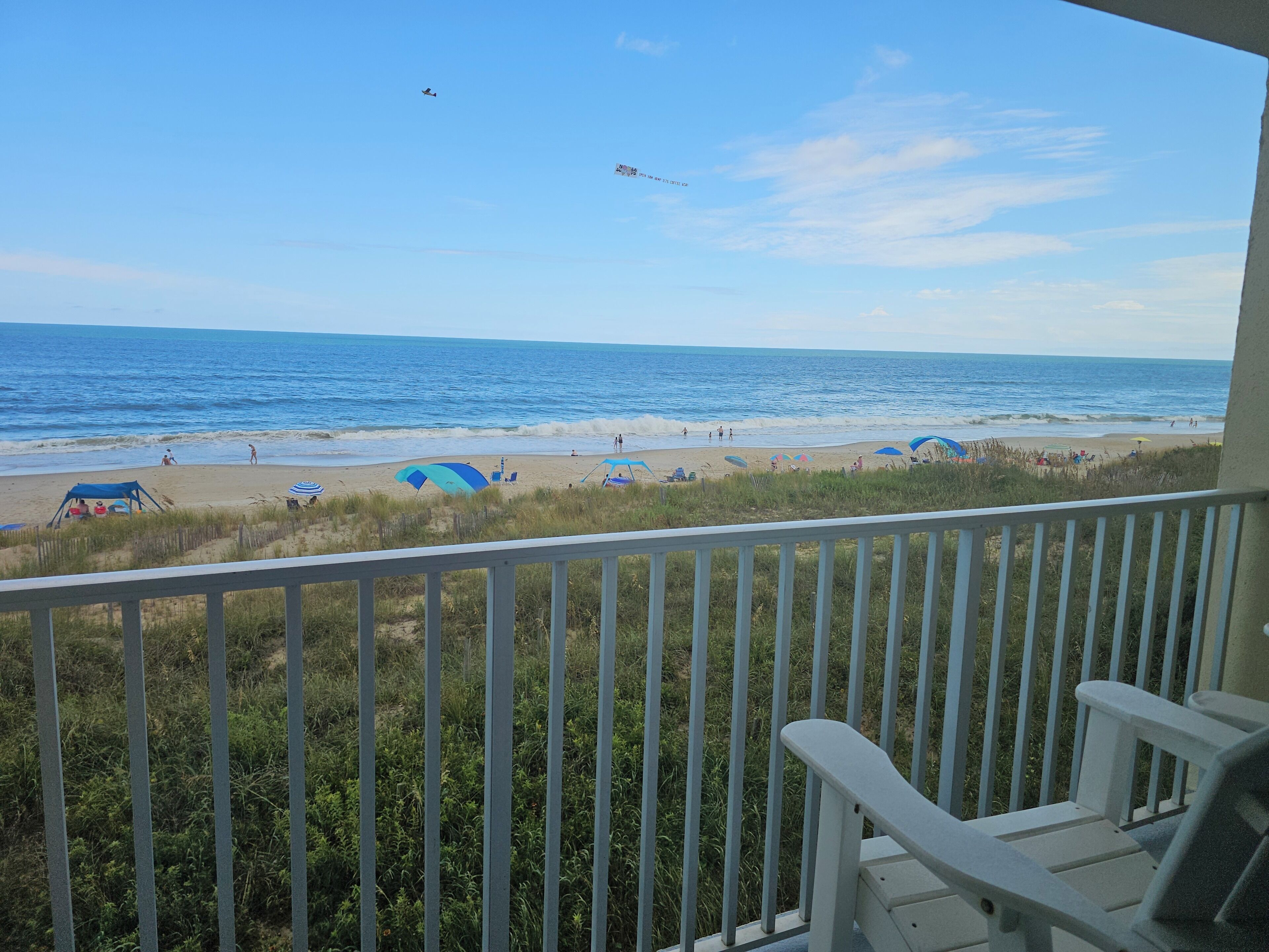 A beach view from a balcony with a railing, beach umbrellas, and a few people on the sand.
