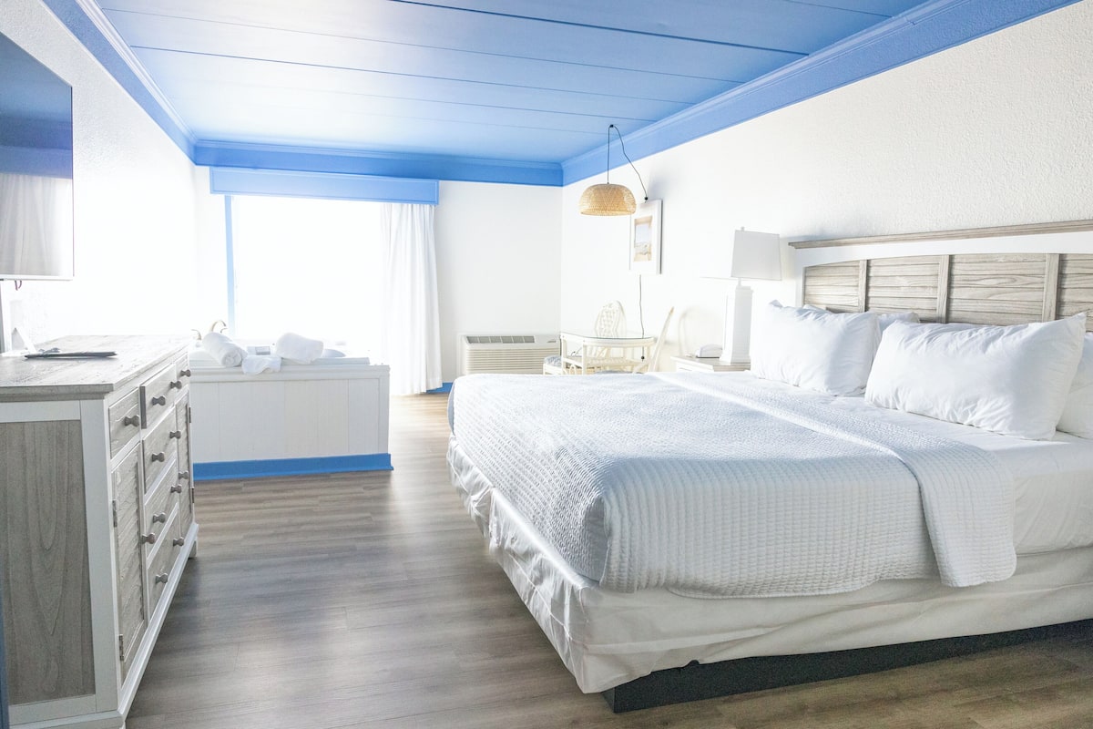 A bedroom with a large bed, a dresser, a chair, and a window with curtains.