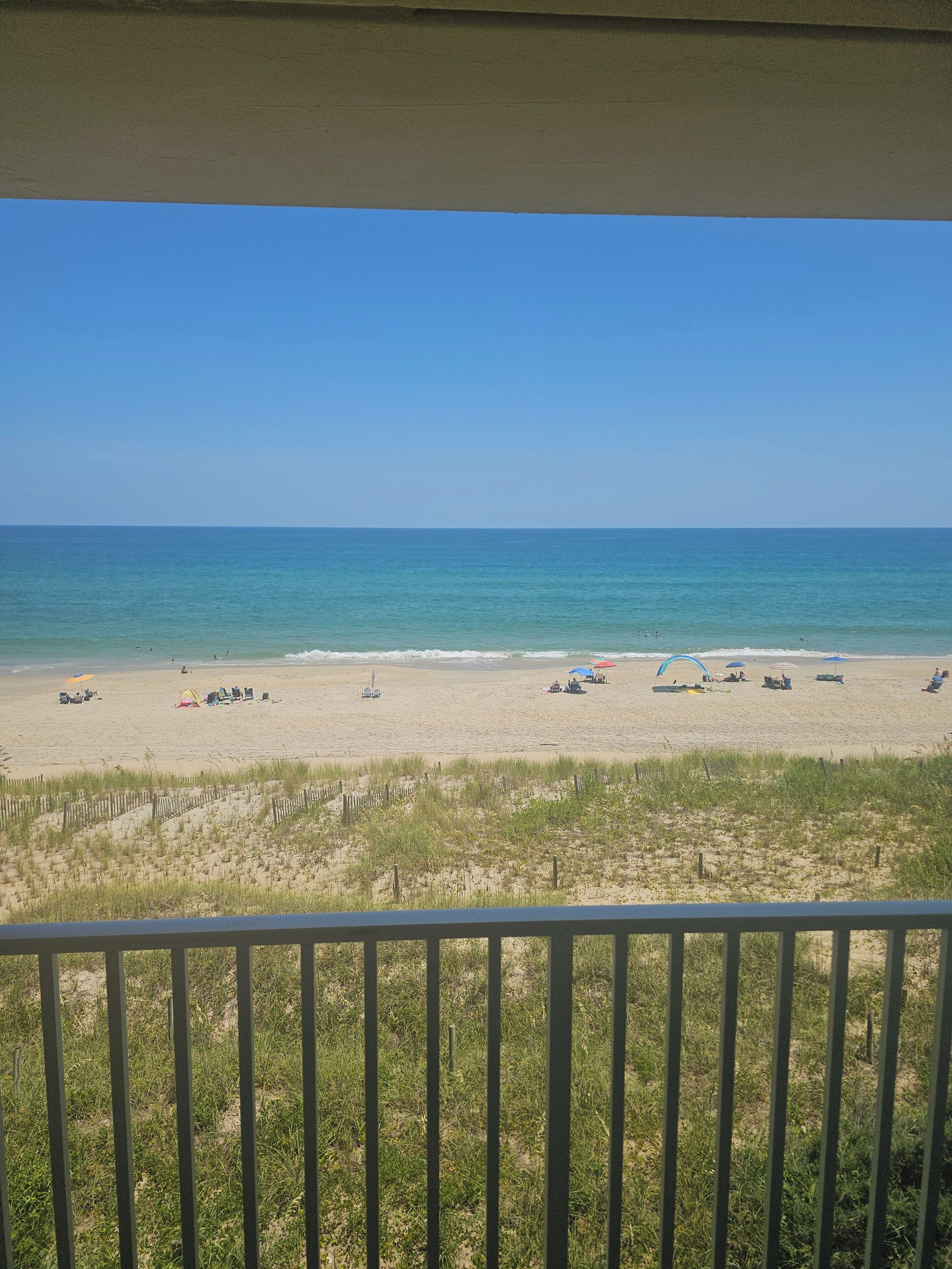 A beach view from a balcony with a railing, sandy beach, and ocean.