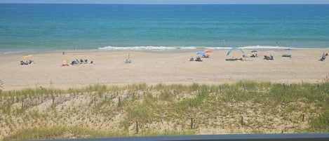 A beach view from a balcony with a railing, sandy beach, and ocean.