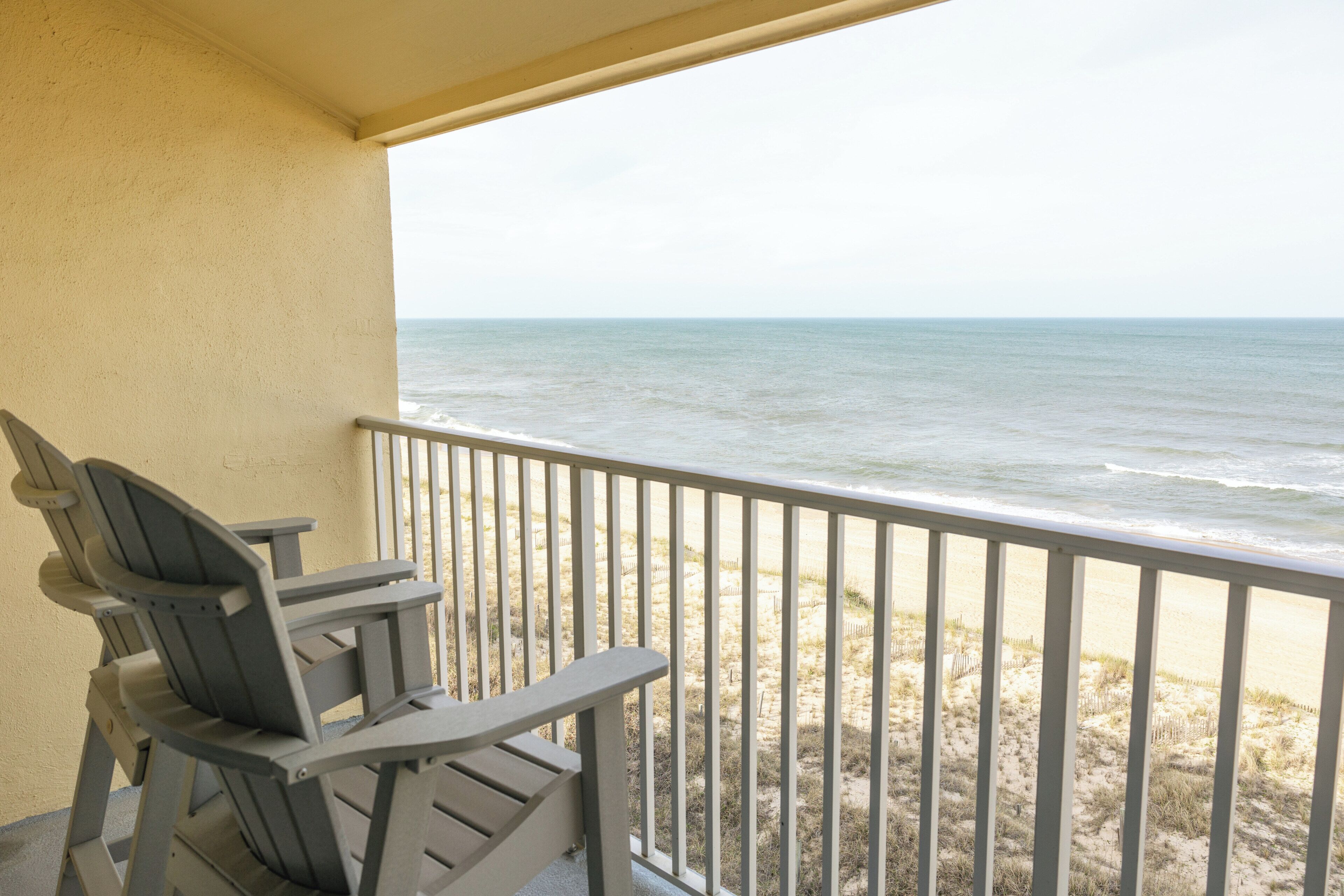 A balcony with a view of the ocean, a chair, and a railing.