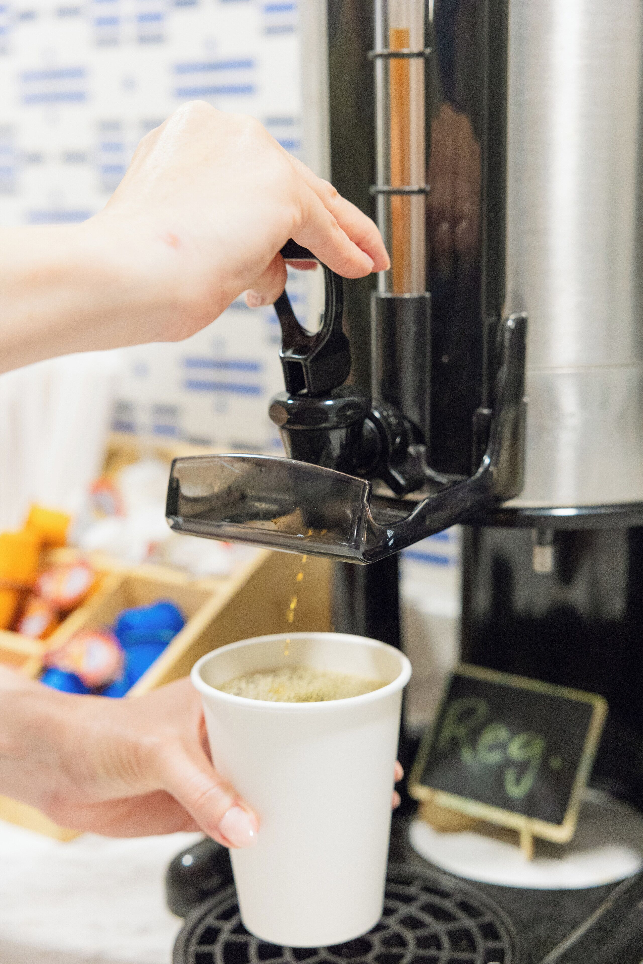 Una mano sosteniendo una taza debajo de un dispensador de café, con un letrero que dice 'Reg'.