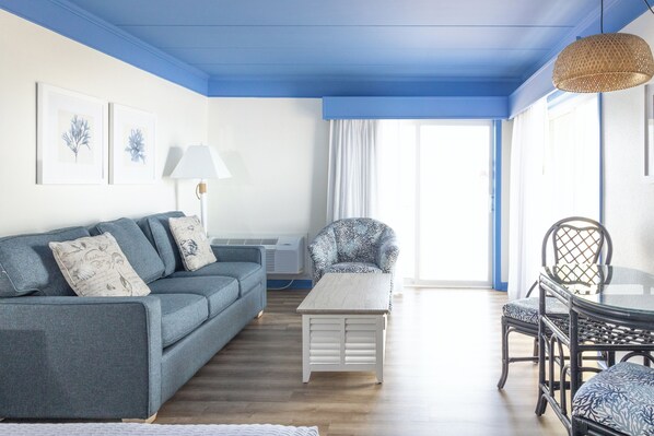 A living room with a sofa, a small table, a chair, and a dining table with chairs.