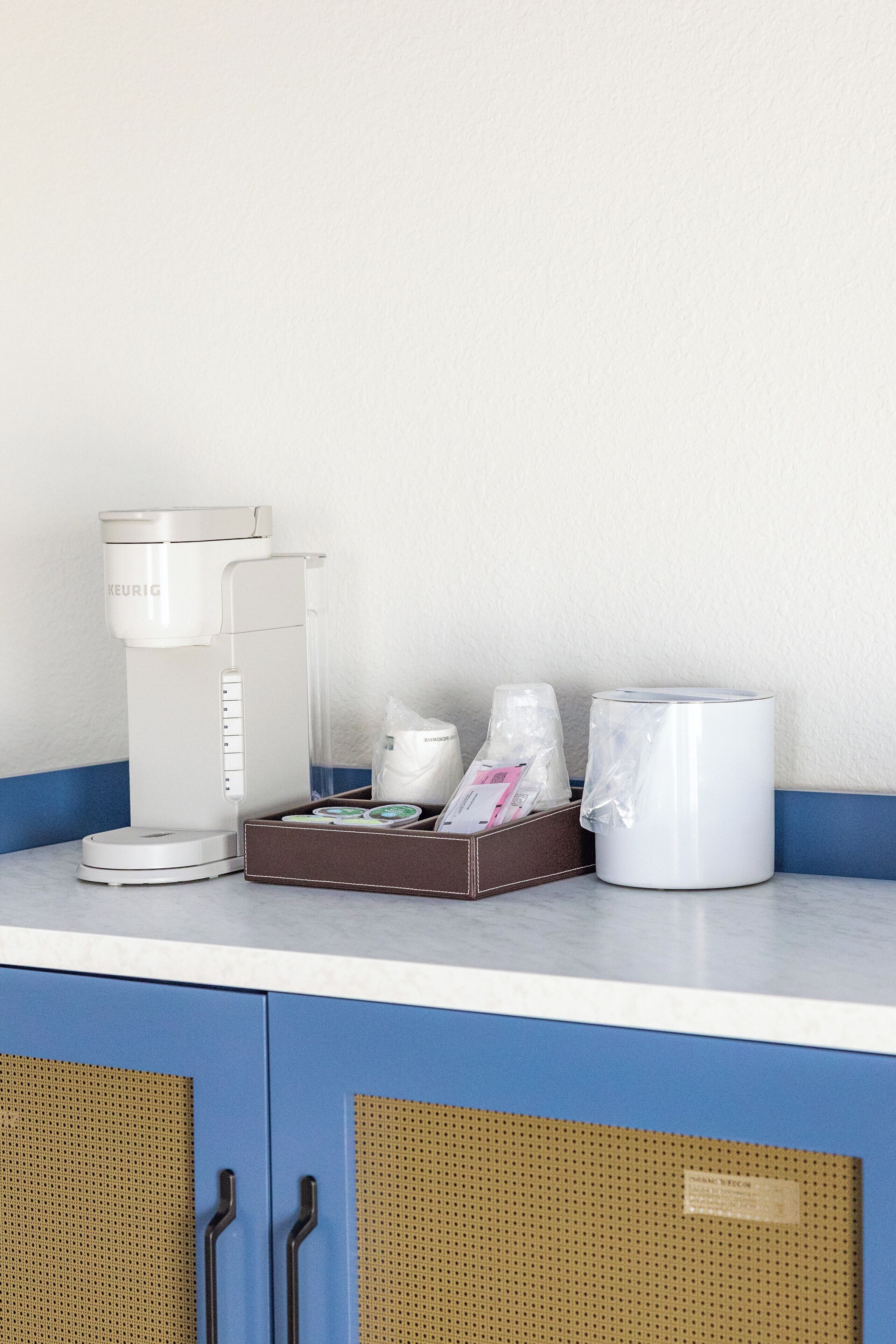 Een koffiezetapparaat, een doos met koffiekapsules, een waterdispenser en een koffiekan op een aanrecht.