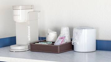 A coffee maker, a box with coffee pods, a water dispenser, and a coffee pot on a counter.