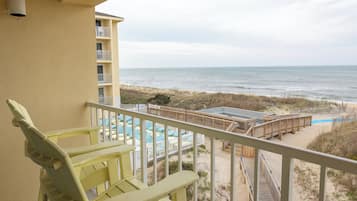 A balcony with a view of the beach, a pool area, and a wooden deck.
