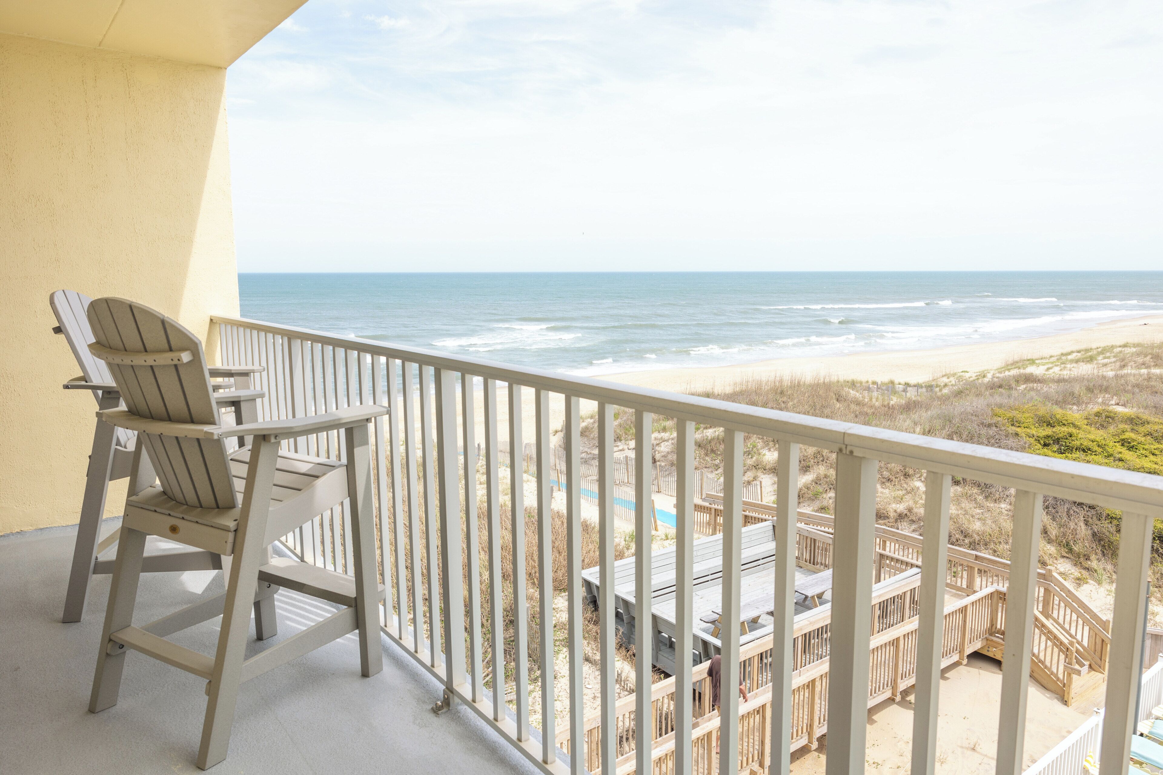 A balcony with a view of the beach, a chair, and a wooden deck.