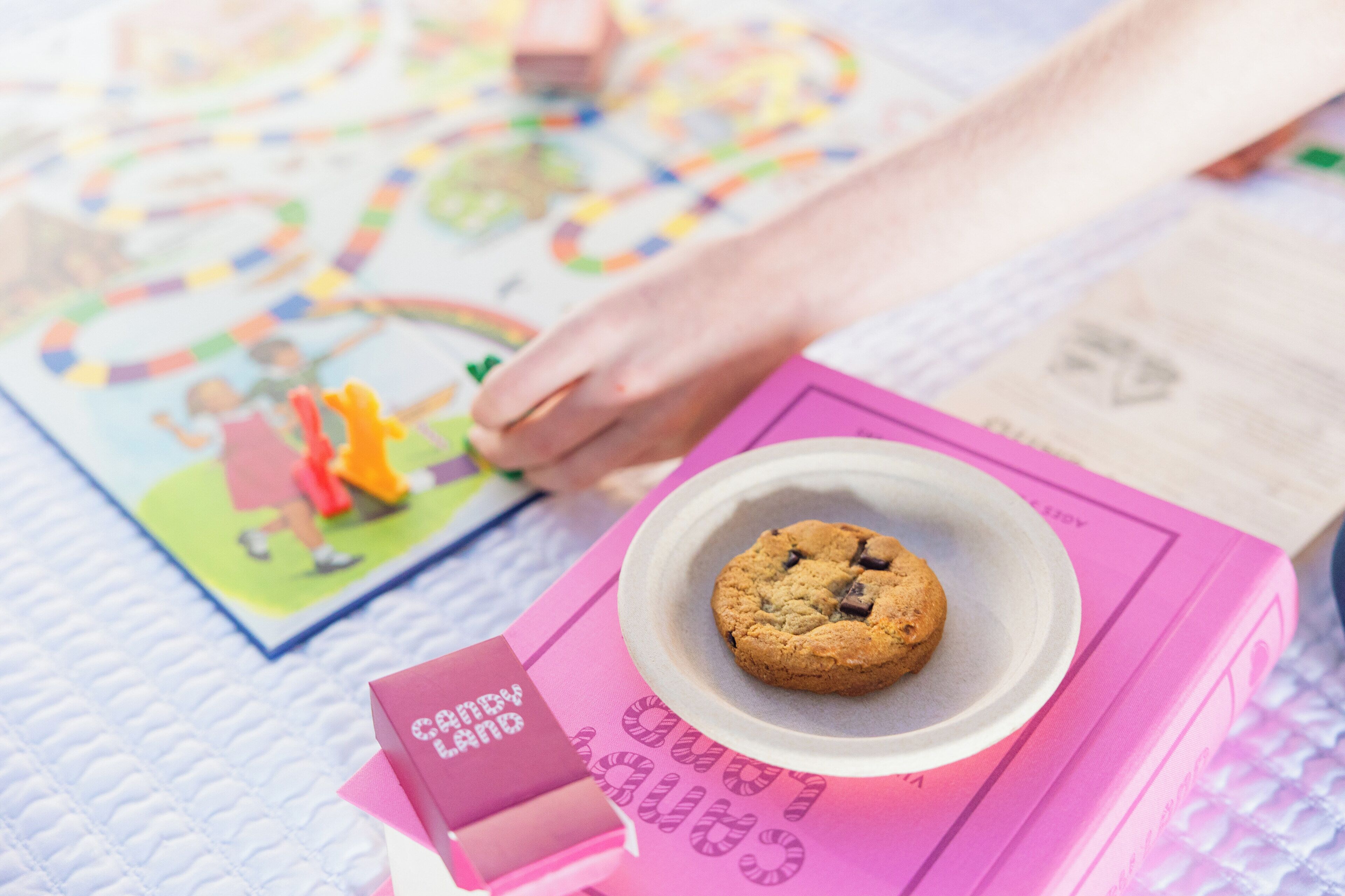 A cookie on a pink box with a label, a hand, and a board game on a textured surface.