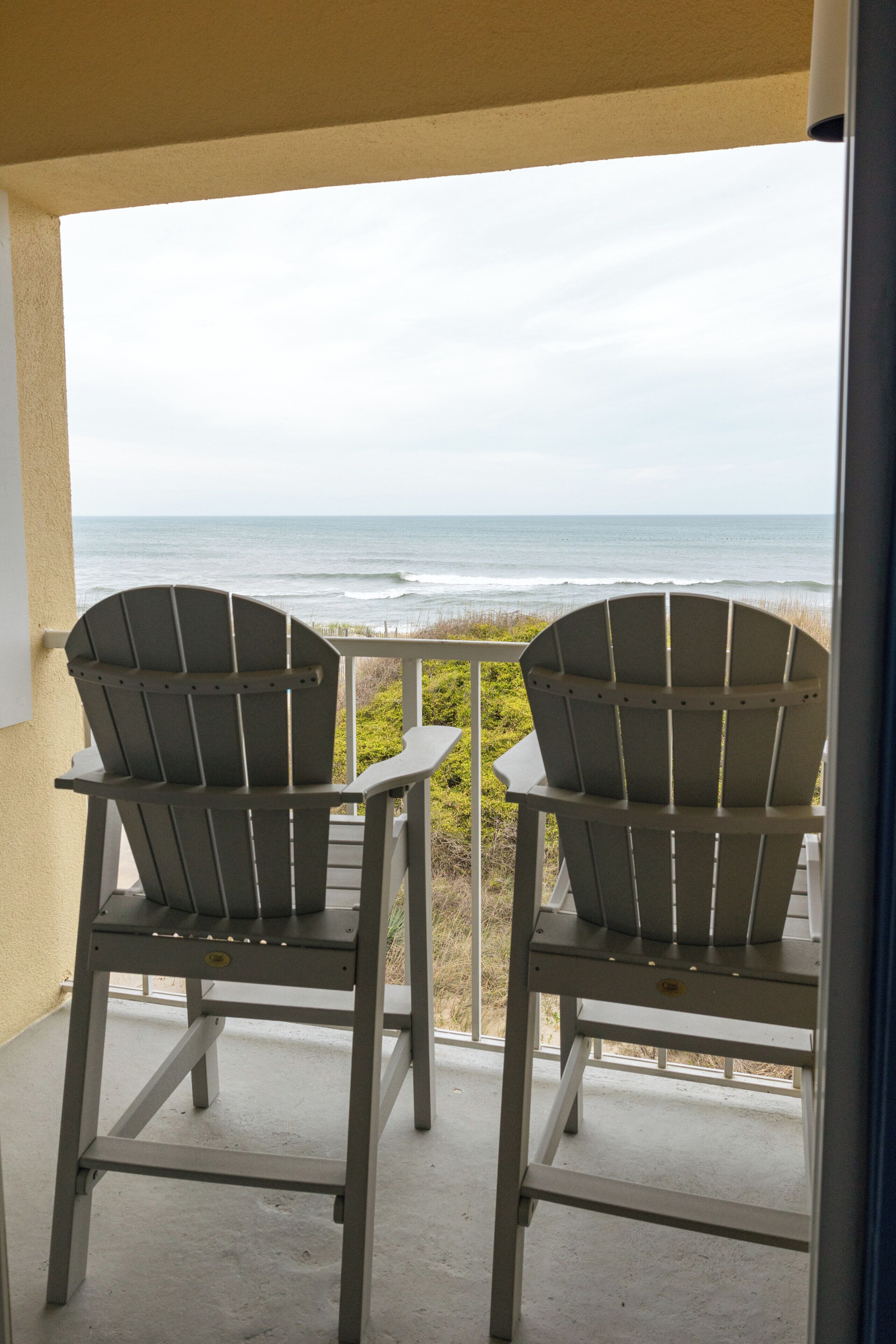 Two Adirondack chairs on a balcony with a view of the ocean.