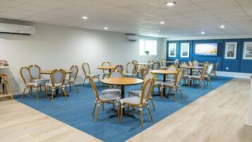 A conference room with round tables and chairs, air conditioning units, and framed pictures on the walls.