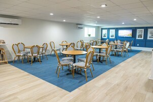 Una sala de conferencias con mesas y sillas redondas, unidades de aire acondicionado y cuadros en las paredes.