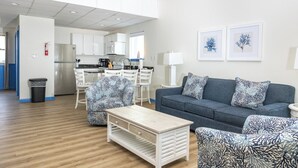 A modern living room with a grey sofa, patterned armchairs, a wooden coffee table, and a kitchen in the background. - Surf Side Hotel (Nags Head)
