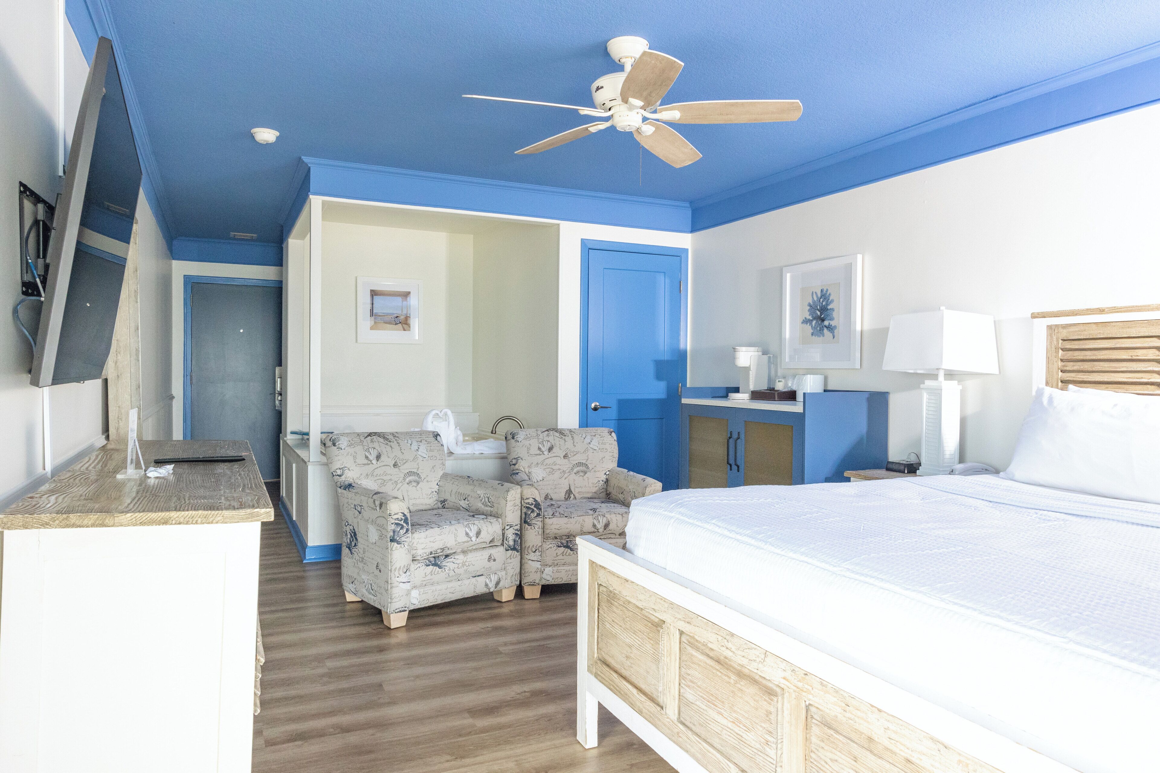 Un dormitorio con cama, ventilador de techo, escritorio, silla y baño.