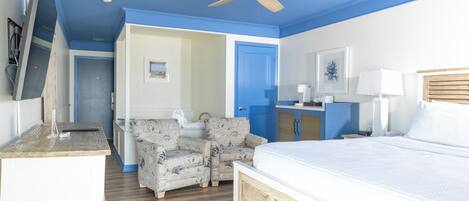 Un dormitorio con cama, ventilador de techo, escritorio, silla y baño.