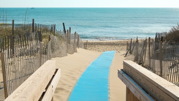 A wooden boardwalk leading to a beach with a blue mat on the sand. - Surf Side Hotel (Nags Head)