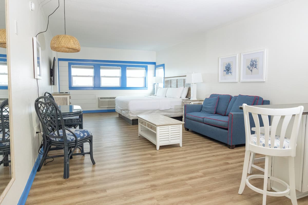 A room with a bed, a sofa, a dining table with chairs, and a small white table.