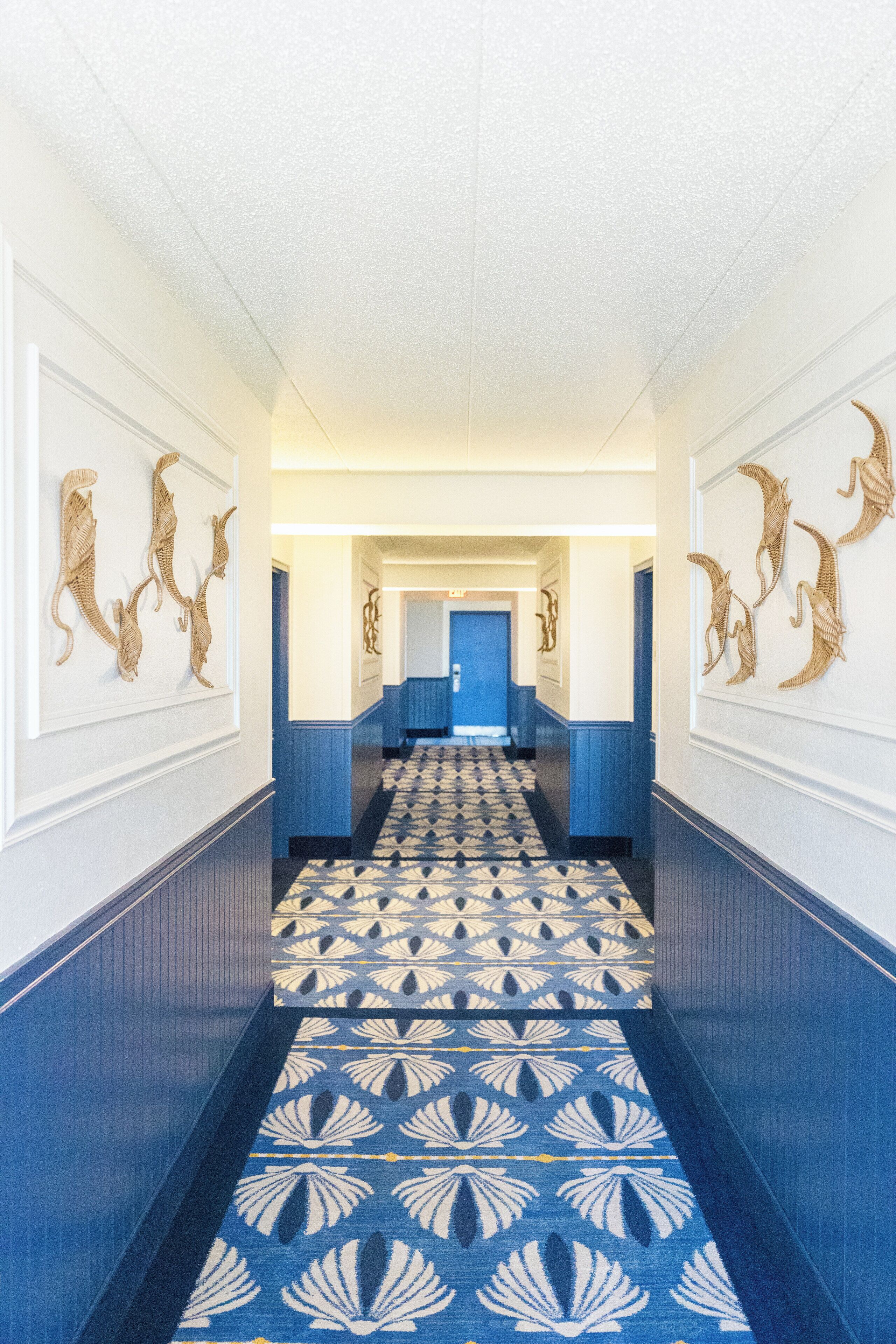 A hallway with patterned carpet, blue walls, and wall-mounted artwork.