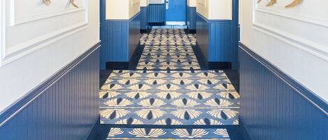 A hallway with patterned carpet, blue walls, and wall-mounted artwork.
