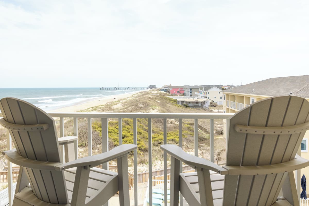 A balcony with two Adirondack chairs overlooking a beach and ocean.