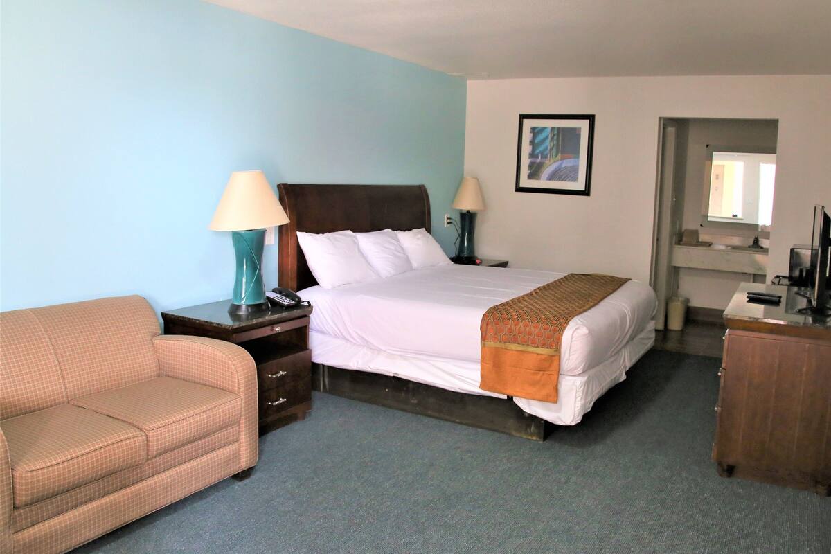 Una habitación de hotel con una cama, dos mesitas de noche, una lámpara, un sofá y un aparador.