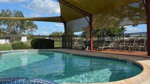 Una piscina con zona techada y sillas de descanso.