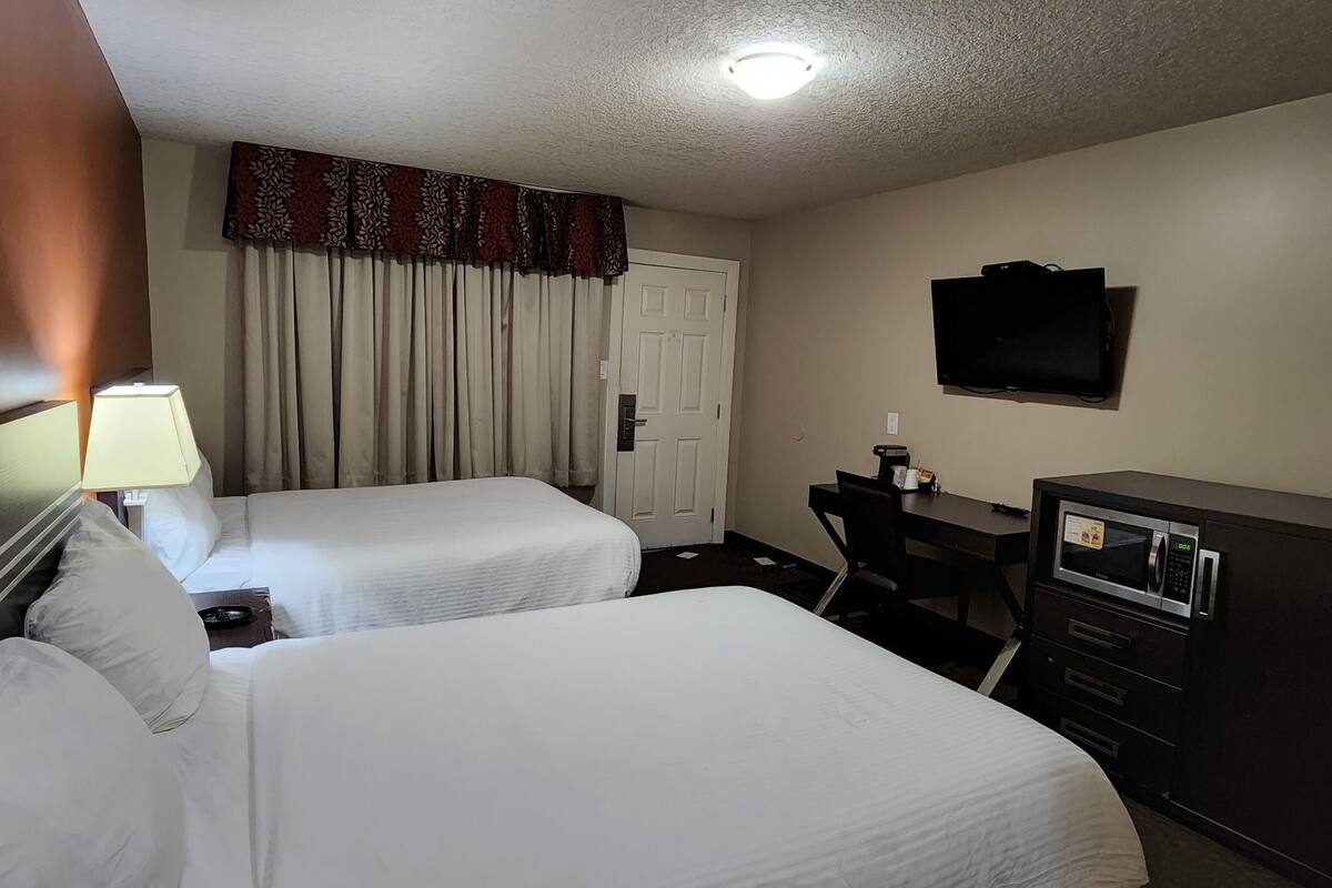 A hotel room with two beds, a desk, a television, and a minibar.
