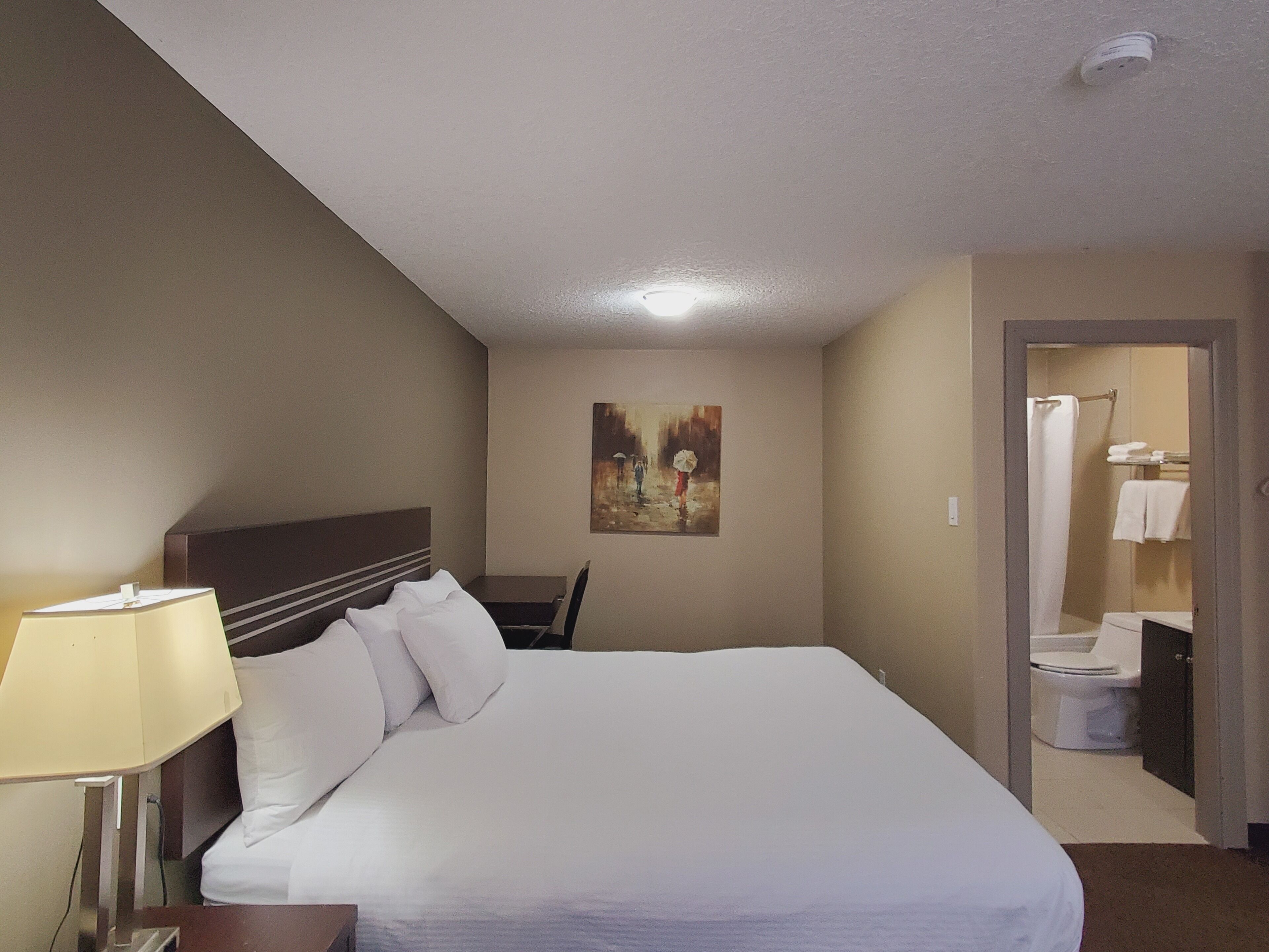 Een hotelkamer met een bed, een schilderij aan de muur, en een badkamer zichtbaar door een geopende deur.