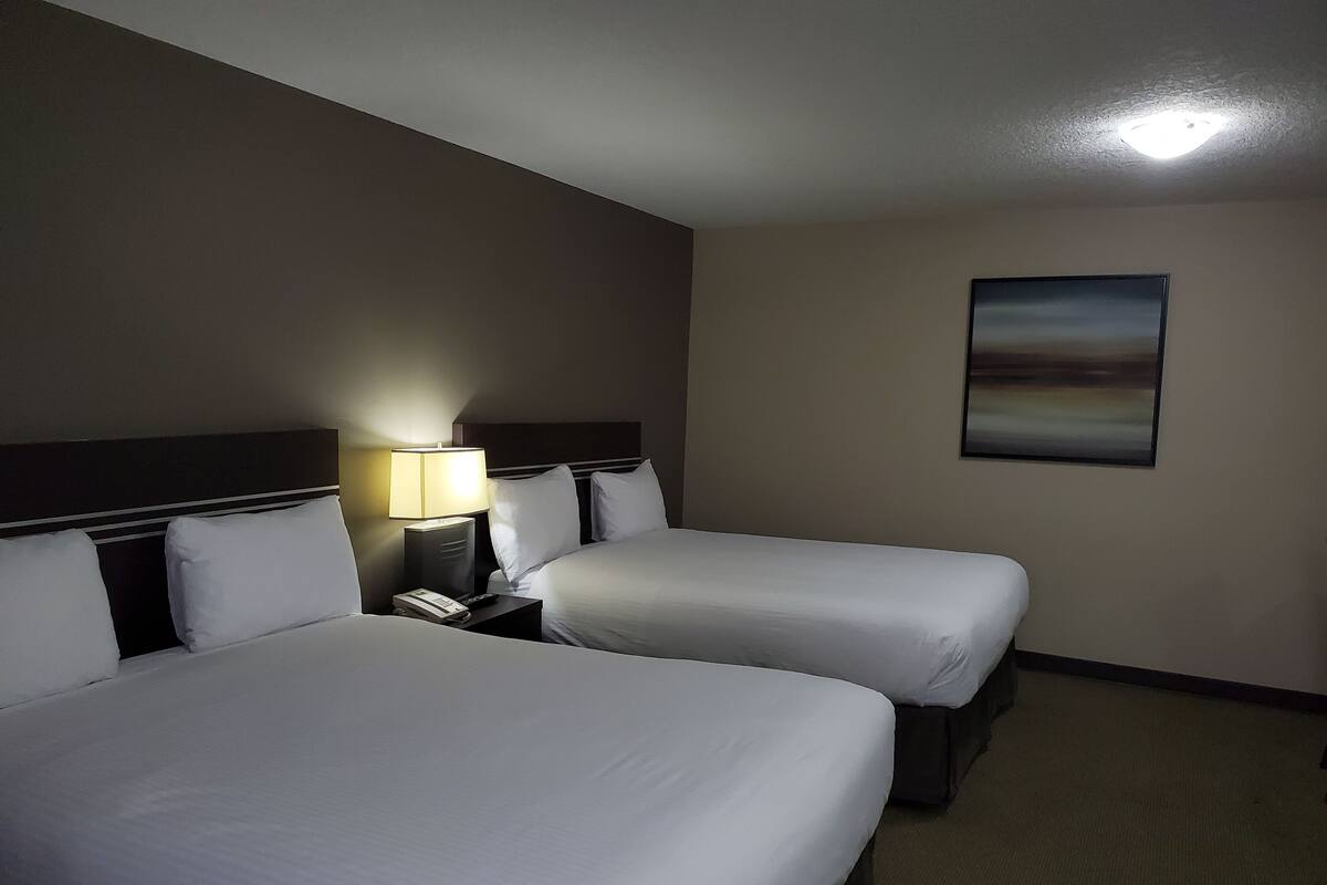 A hotel room with two beds, a nightstand with a lamp, a phone, and a painting on the wall.