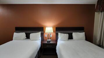 A hotel room with two beds, a nightstand with a lamp, and a window with curtains.