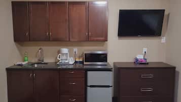 Cocina pequeña con armarios de madera, microondas integrado, refrigerador y televisor de pantalla plana montado en la pared.