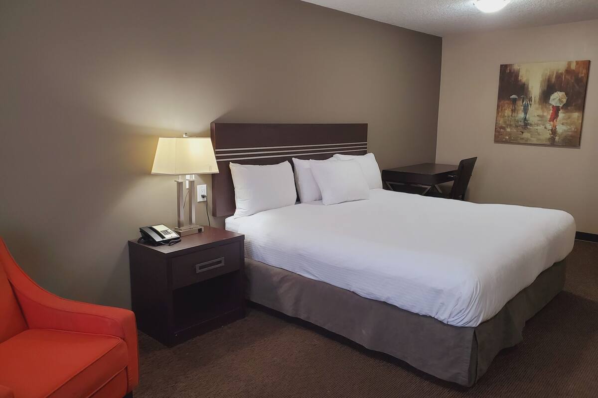 A hotel room with a bed, a nightstand with a lamp, a telephone, a small table, and a chair.
