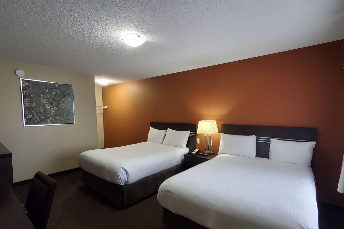 A hotel room with two beds, a desk, and a nightstand with a lamp.