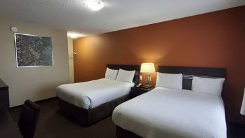 Une chambre d’hôtel avec deux lits, un bureau et une table de chevet avec une lampe.