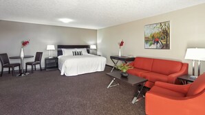 A hotel room with a bed, a red sofa, a desk, and a chair. - Royal Lodge (Edmonton)