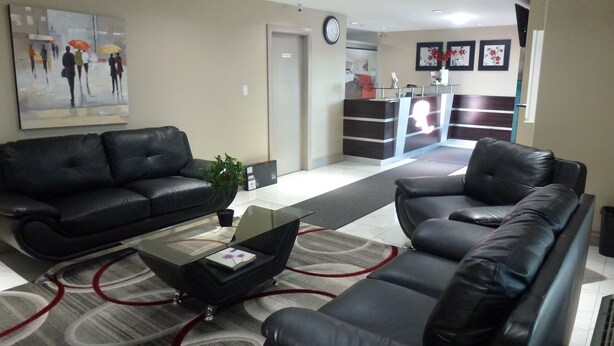 A modern lobby with black leather sofas, a glass coffee table, and a reception desk. - Royal Lodge (Edmonton)