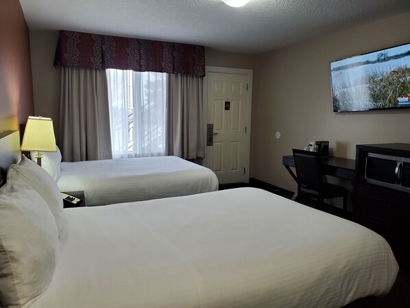 Habitación de hotel con dos camas, un escritorio, un televisor y una ventana con cortinas.