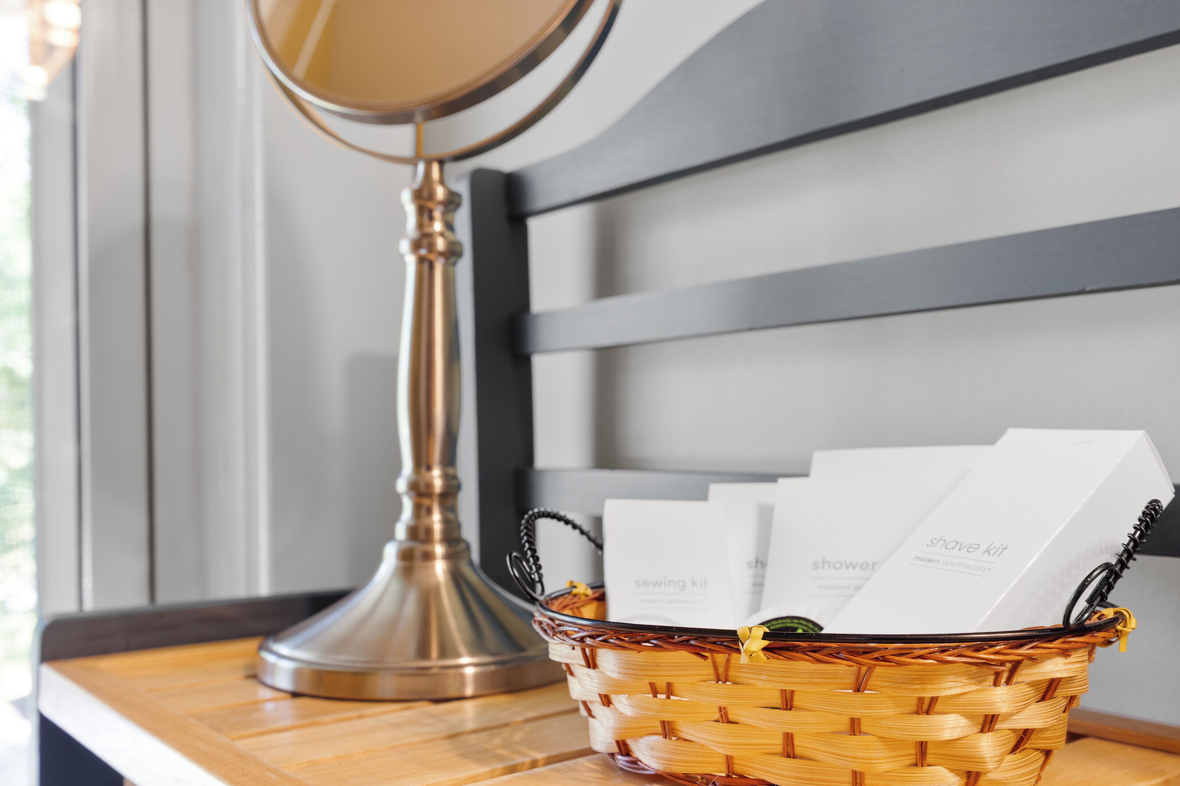 A wicker basket with shaver kits and a compact mirror on a wooden surface.