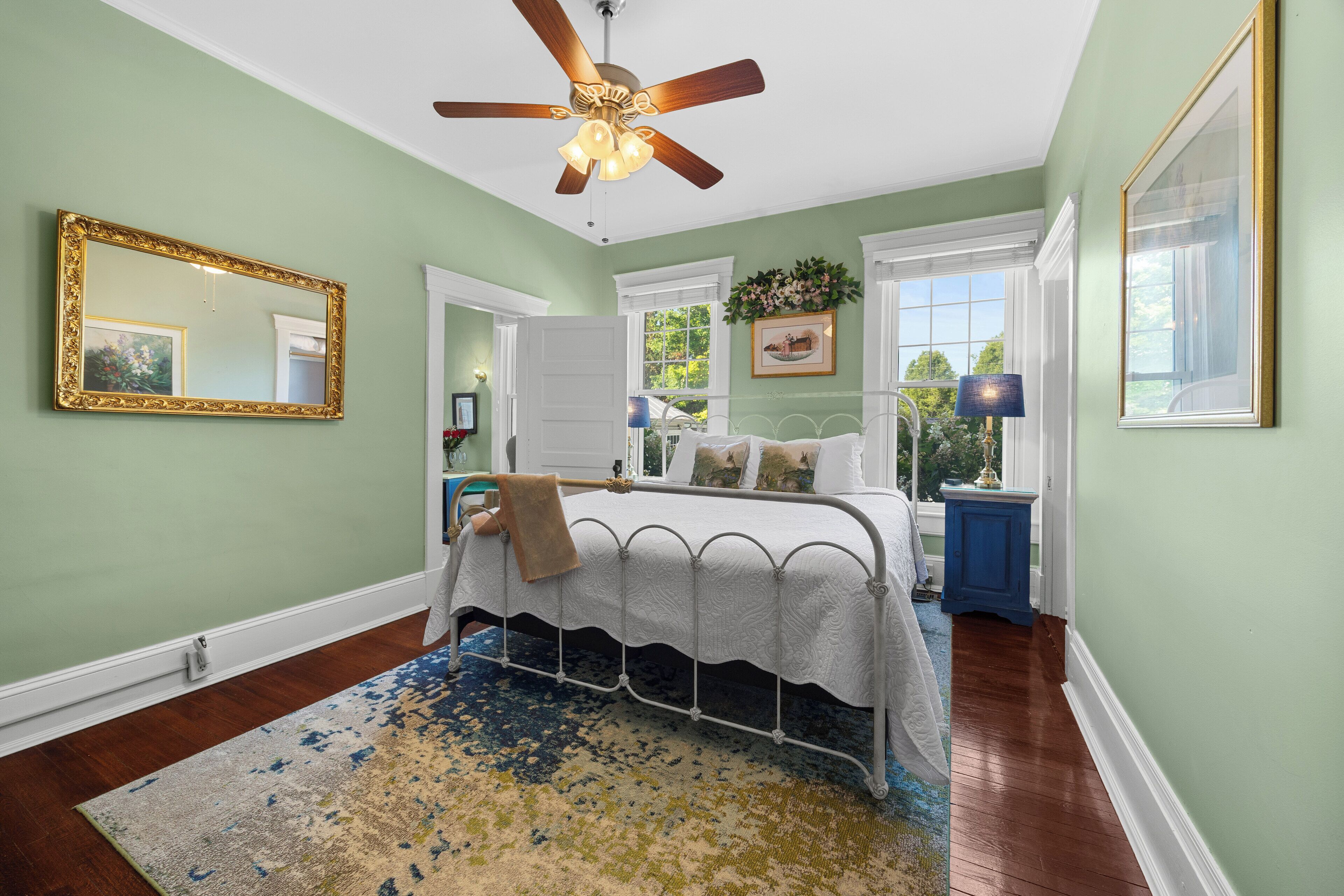 A bedroom with a bed, a ceiling fan, a large mirror, and a window.