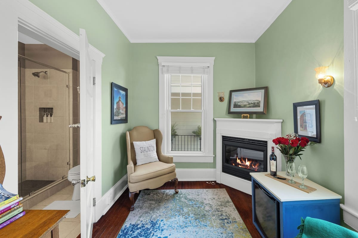A well-lit living room with a fireplace, a comfortable armchair, and a bookshelf.