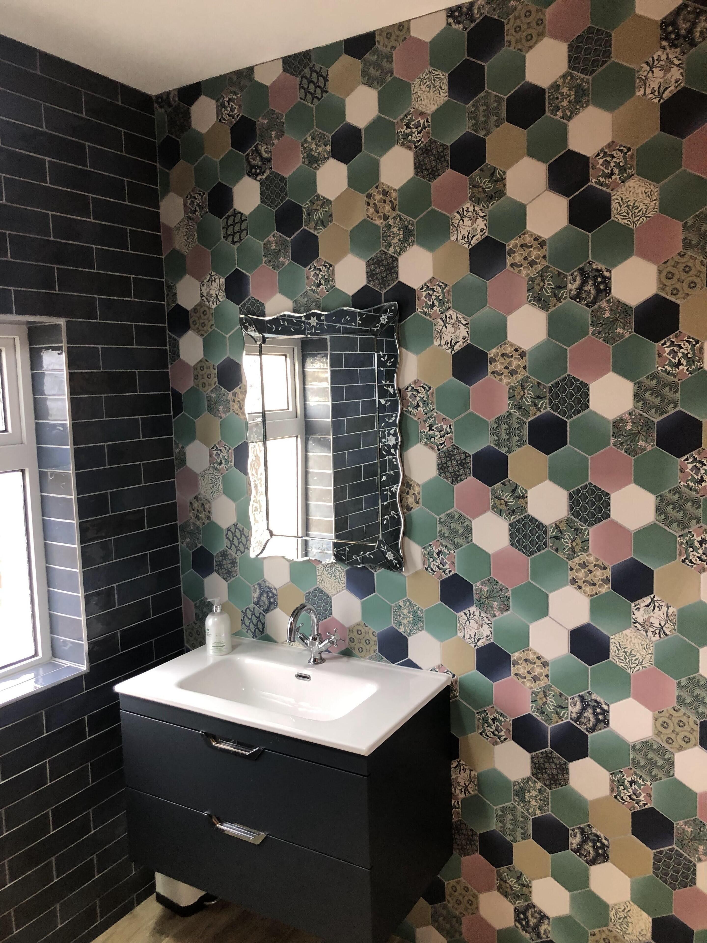 Une salle de bain avec un mur recouvert de carreaux noirs, un lavabo blanc et un miroir.