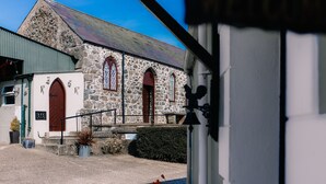 A stone church with arched windows and a red door. - Brookhall Cottages (Lisburn)