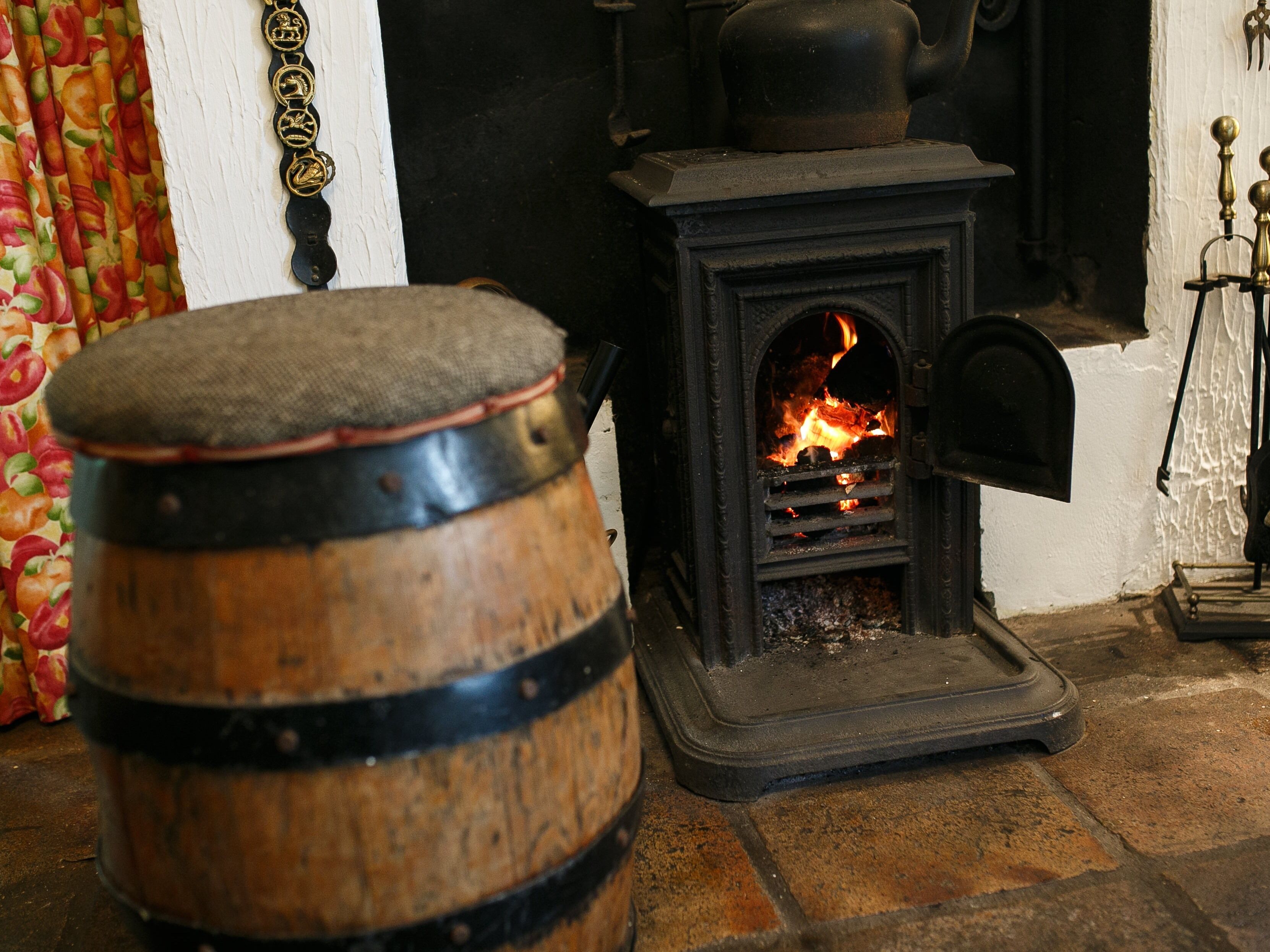 Un barril de madera, una estufa negra con fuego y una puerta con cortina.