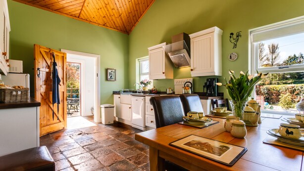 A kitchen with a wooden ceiling, green walls, and a dining area with a table and chairs. - Brookhall Cottages (Lisburn)