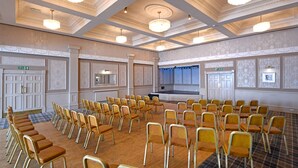 A conference room with rows of chairs, a stage, and chandeliers. - Corner House Hotel (Annan)