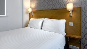 A hotel room with a large bed, two bedside lamps, and a patterned wall. - Corner House Hotel (Annan)